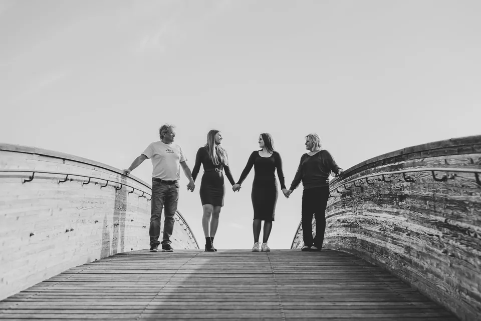 Černobílá rodinná fotografie, čtyři lidé se drží za ruce na dřevěné lávce