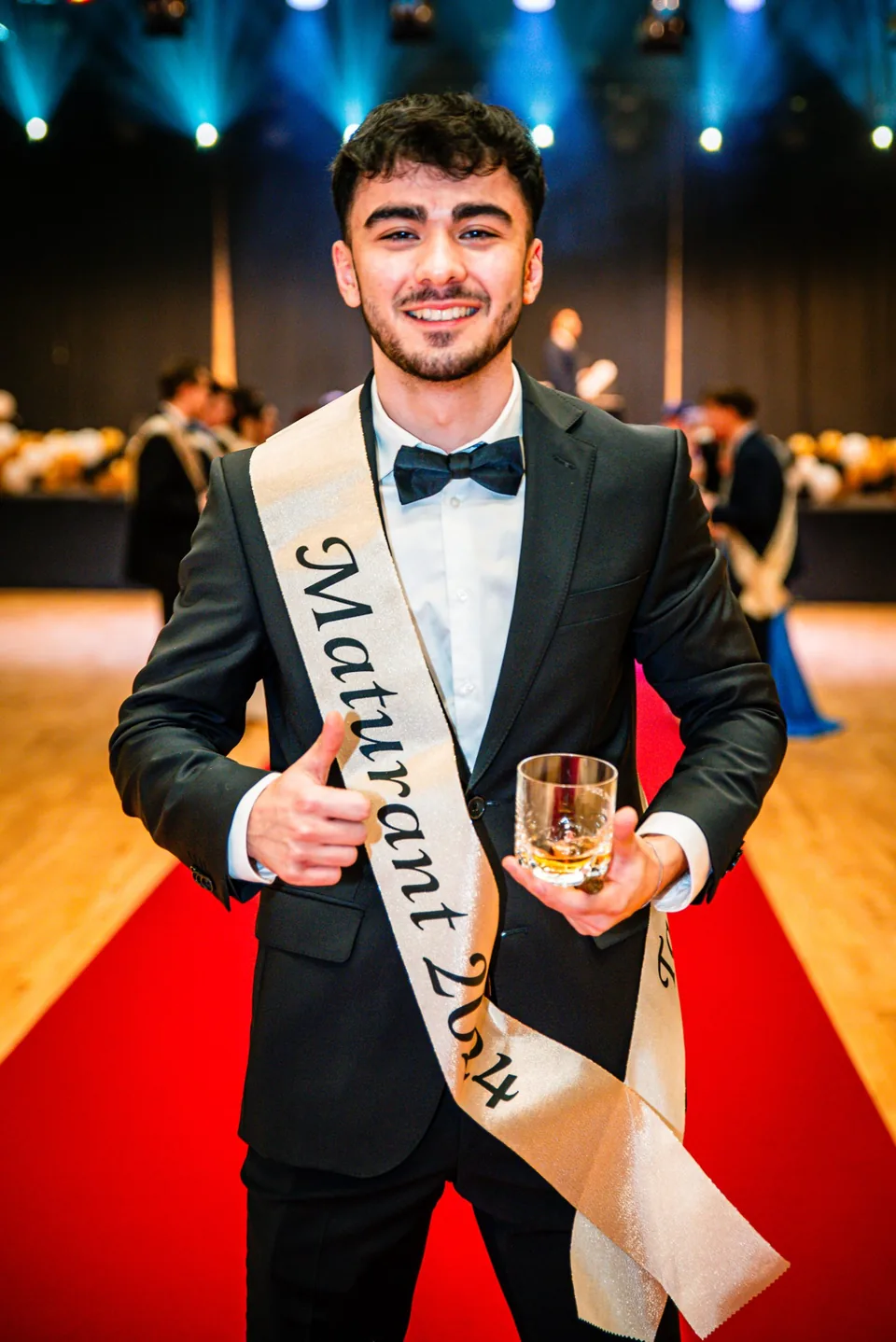 Maturant v obleku se šerpou a sklenkou na plese